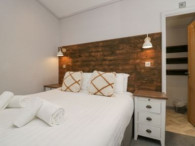 A bedroom with a bed with white linens and pillows with a wooden headboard and two bedside tables at The Bothy in Keswick