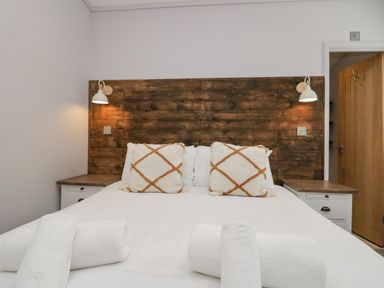 A bedroom with a bed with white sheets and two patterned pillows two bedside tables with lamps and a wooden door at The Bothy in Keswick