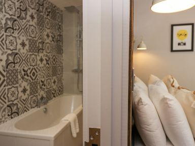 A bathroom with a bathtub and patterned wall tiles next to a bedroom with pillows and wall art at The Bothy in Keswick
