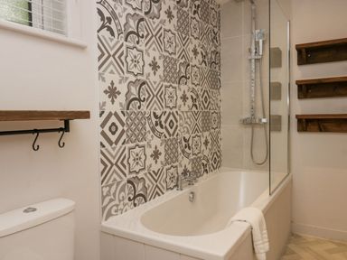 A bathroom with a bathtub shower with patterned tiles wooden shelves and a towel at The Bothy in Keswick