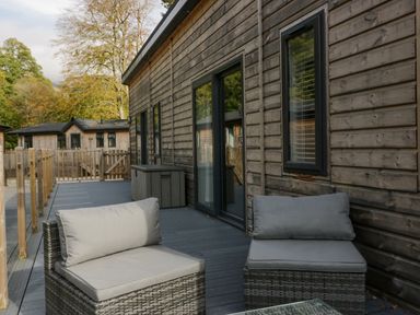An outdoor wooden deck with two cushioned wicker chairs and a storage box at The Bothy in Keswick