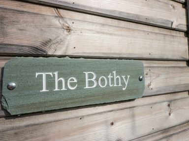 A green stone sign with white letters The Bothy mounted on a wooden wall at The Bothy in Keswick