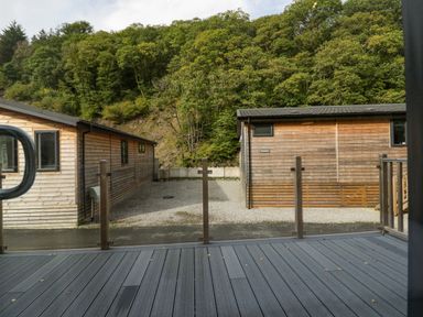 A view of two wooden cabins separated by a gravel area with a forested hill in the background at The Bothy in Keswick