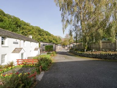 A paved road with white cottages and wooden buildings surrounded by trees and flowers at The Bothy in Keswick