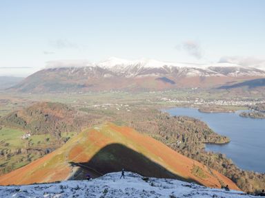 A landscape with a lake fields hills and snow covered mountains in the background at The Bothy in Keswick
