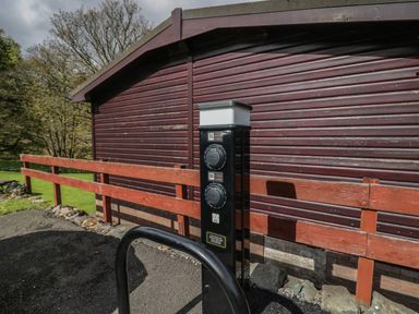 An electric vehicle charging station next to a wooden fence and a brown wooden building wall at The Bothy in Keswick