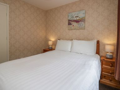 A bedroom with a double bed white bed linen two bedside tables with lamps and a painting on the wall at Apartment 1 in Keswick