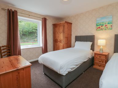 A bedroom with two single beds a wooden wardrobe a wooden desk and a window with curtains at Apartment 1 in Keswick