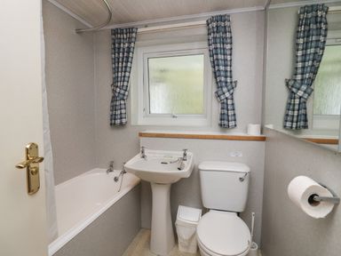 A bathroom with a bathtub sink toilet window and blue checkered curtains at Apartment 1 in Keswick