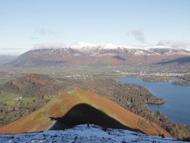 A mountainous landscape with snow on peaks and a lake surrounded by forest and fields at Apartment 1 in Keswick