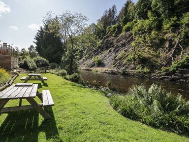 A river running alongside a grassy area with wooden picnic tables and trees at Apartment 2 in Keswick