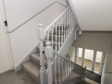 A carpeted staircase with white wooden railings and glass doors at the bottom at Apartment 2 in Keswick