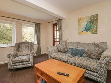 A living room with patterned sofa and armchair wooden coffee table and peacock painting on wall at Apartment 2 in Keswick