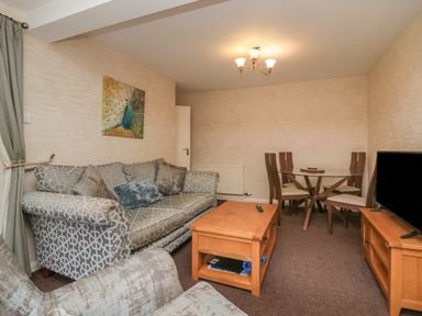 A living room with patterned sofas a wooden coffee table a glass dining table with chairs and a television at Apartment 2 in Keswick