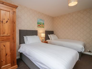 A bedroom with two single beds a wooden wardrobe a bedside table with a lamp and a wall painting at Apartment 2 in Keswick