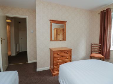A bedroom with a wooden chest of drawers and mirror a wooden chair with cushion near window and a bed at Apartment 2 in Keswick