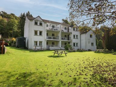 A white three-story residential building with balconies and outdoor seating on a lawn with picnic tables at Apartment 2 in Keswick