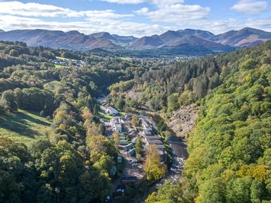 An aerial view of a village situated near a river surrounded by mountains and trees at Apartment 2 in Keswick