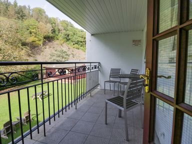 A balcony with metal chairs and table overlooking a grassy yard with picnic tables and trees at Apartment 3 in Keswick