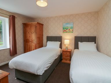 A bedroom with two single beds a wooden wardrobe a bedside table with a lamp and a painting on the wall at Apartment 3 in Keswick