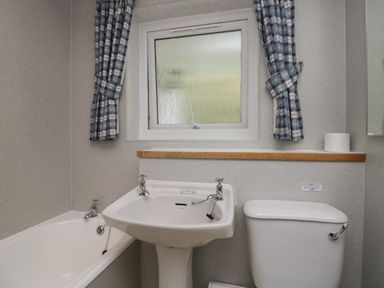 A bathroom with a bathtub a sink and a toilet under a window with curtains at Apartment 3 in Keswick