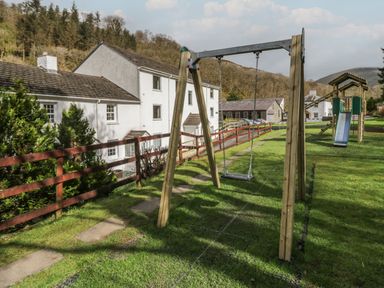 A playground with a wooden swing set and slide next to white houses and trees at Apartment 3 in Keswick