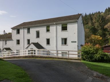 A three-story white building with multiple windows surrounded by trees and grass at Bobbin Mill in Keswick
