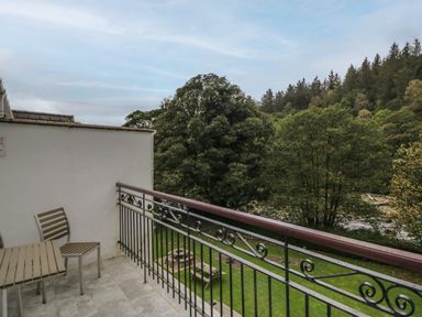 A balcony with table and chair overlooking trees and grassy area at Apartment 4 in Keswick