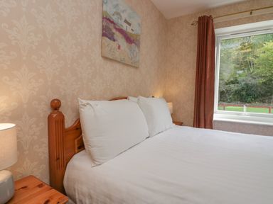 A bedroom with a double bed white pillows and bedding wooden bedside tables with lamps and a window with red curtains at Apartment 4 in Keswick