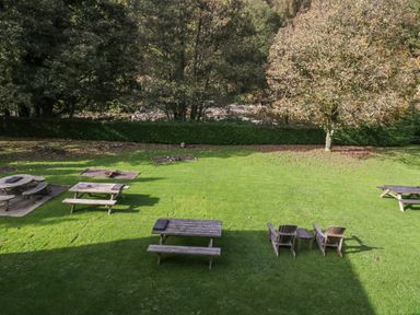 An outdoor grassy area with wooden picnic tables and chairs near trees and a river at Apartment 4 in Keswick