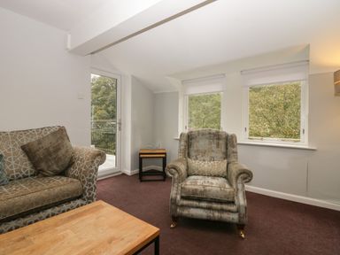 A living room with an armchair a sofa a wooden coffee table and two windows at Apartment 6 in Keswick
