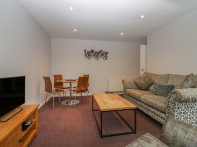 A living room with a patterned sofa wooden coffee table dining table with four chairs and a television on a wooden stand at Apartment 6 in Keswick