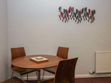 A dining area with a round wooden table and four wooden chairs with a decorative wall art above and a radiator on the wall at Apartment 6 in Keswick