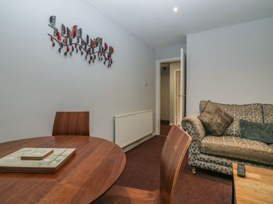 A dining area with wooden chairs a round wooden table and a patterned sofa with cushions at Apartment 6 in Keswick
