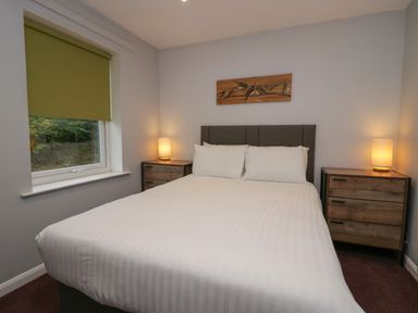 A bedroom with a double bed between two wooden bedside tables with lamps and a window with a green blind at Apartment 6 in Keswick