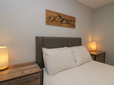 A bedroom with a bed between two wooden nightstands each with a lamp and a bird painting on the wall at Apartment 6 in Keswick