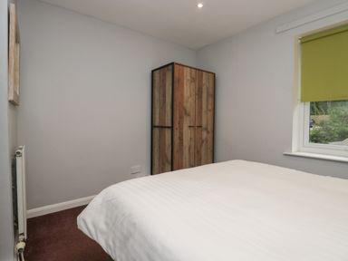 A bedroom with a bed a wooden wardrobe a radiator and a window with a green blind at Apartment 6 in Keswick