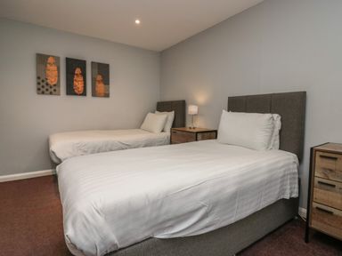 A bedroom with two single beds bedside tables a lamp and three paintings on the wall at Apartment 6 in Keswick