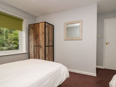 A bedroom with a bed a wooden wardrobe a wall mirror and a window with a green blind at Apartment 6 Keswick
