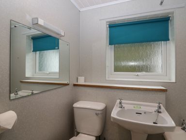 A bathroom with a toilet sink mirror window with blue blind and toilet paper at Apartment 6 in Keswick