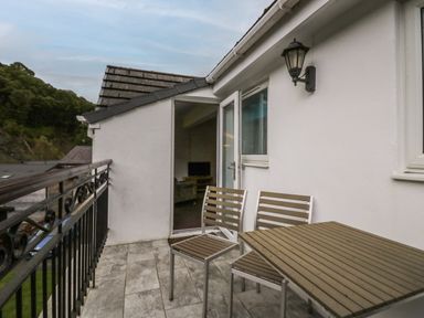 A balcony with two chairs and a table next to a white wall with a light fixture at Apartment 6 in Keswick