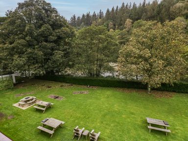 An outdoor grassy area with multiple wooden picnic tables and chairs surrounded by trees at Apartment 6 in Keswick