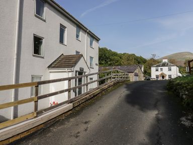 A driveway leading up to white buildings and stone structures with trees and hills in the background at Apartment 6 in Keswick
