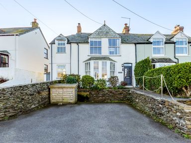 A front view of a white terraced house with bay windows stone walls and a paved driveway at Tre Lowen in Port Isaac