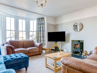 A living room with brown leather sofas a blue ottoman wooden coffee table a television on a wooden tripod stand and a fireplace at Tre Lowen in Port Isaac
