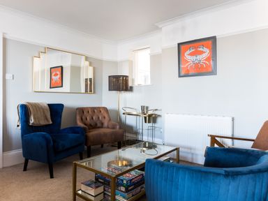 A living room with blue and brown chairs a glass coffee table with board games and a crab picture on the wall at Tre Lowen in Port Isaac