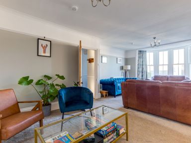 A living room with a glass coffee table holding board games two armchairs a leather sofa and a large window with curtains at Tre Lowen in Port Isaac