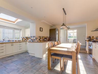 A kitchen with a wooden dining table and chairs tiled floors and multi colored tiled walls at Tre Lowen in Port Isaac