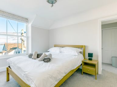 A bedroom with a bed wooden frame and white bedding with rolled towels on top and a wooden bedside table with a lamp at Tre Lowen in Port Isaac