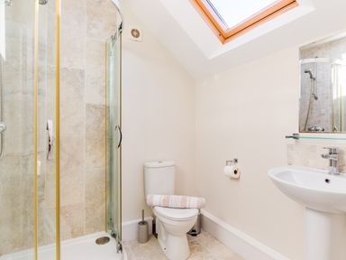 A bathroom with a glass shower enclosure a toilet with a towel on it and a sink under a skylight at Tre Lowen in Port Isaac